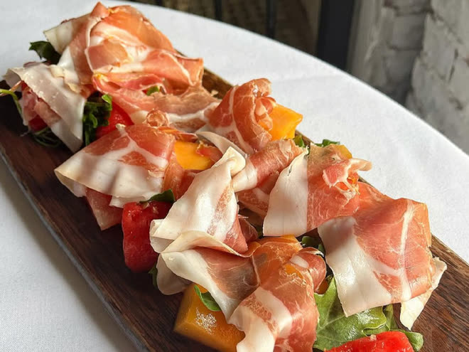 Slices of prosciutto and coppa with melon and rocket on a wooden board.