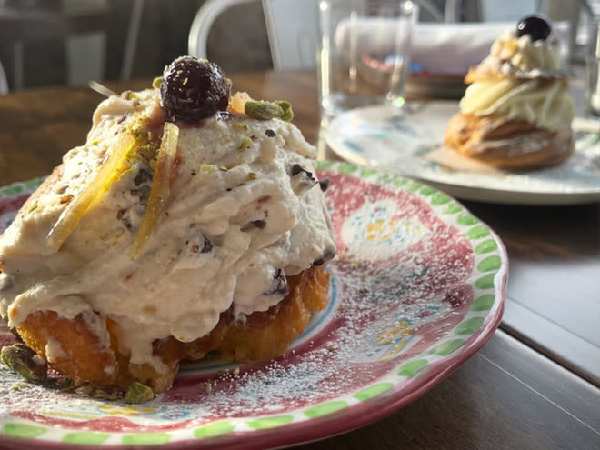 A cream-filled pastry with pistachio and candied peel on a painted plate.