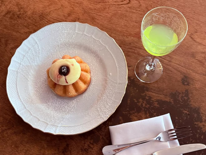 A small cream tart on white china beside a green cocktail, seen from above.