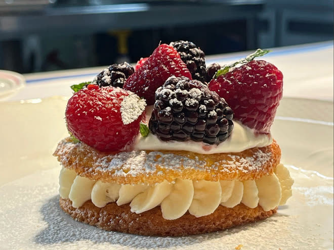 A layered cream pastry topped with raspberries and blackberries under icing sugar.