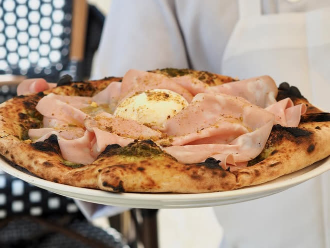 A pizza folded with mortadella and burrata, carried out by a chef in whites.