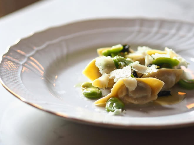 Ravioli with broad beans and shaved cheese on a fluted white plate.
