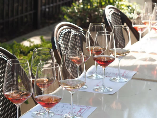 A row of filled wine glasses running down a white table in the sun.