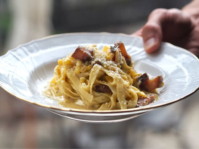 A bowl of tagliatelle with guanciale and grated cheese, carried to the table.