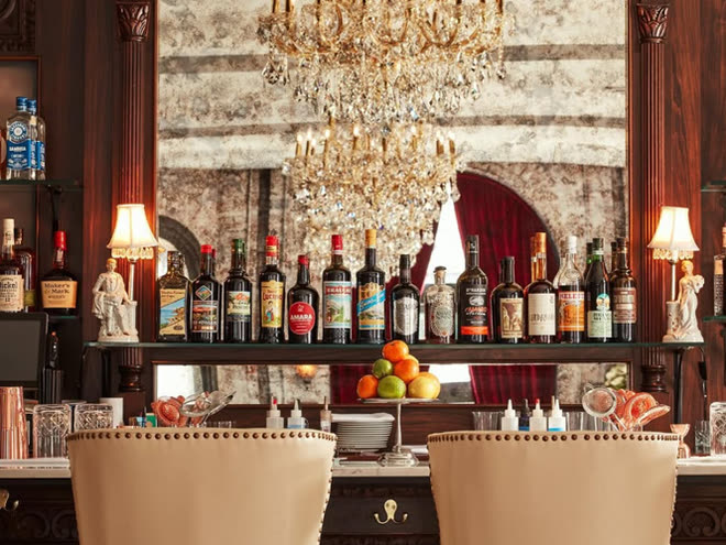 A marble bar beneath a crystal chandelier, its shelves lined with bottles.