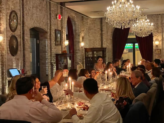 A long candlelit table of guests raising glasses beneath crystal chandeliers.