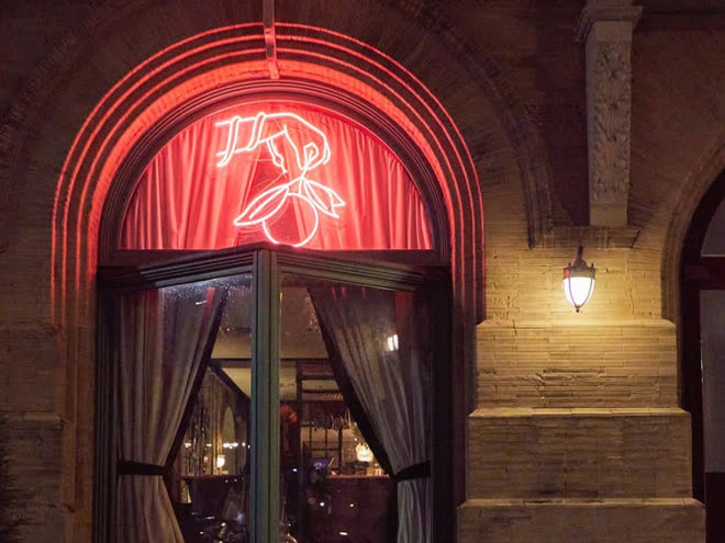 A red neon cicada glowing above an arched doorway.