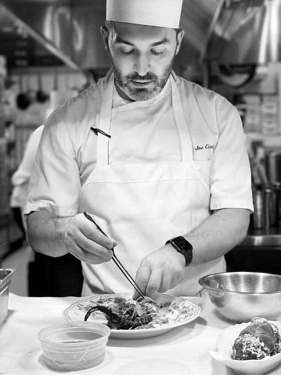 Chef Joe Cicala plating a dish at the pass, in his whites.