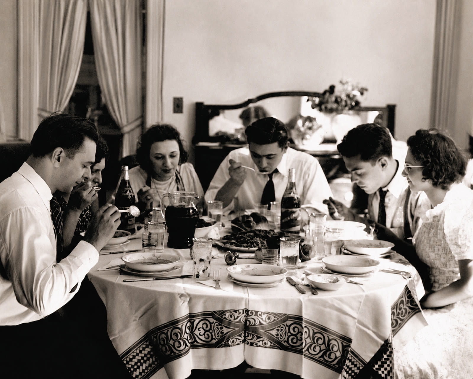 A family gathered around a laid dinner table, photographed in the mid-twentieth century.