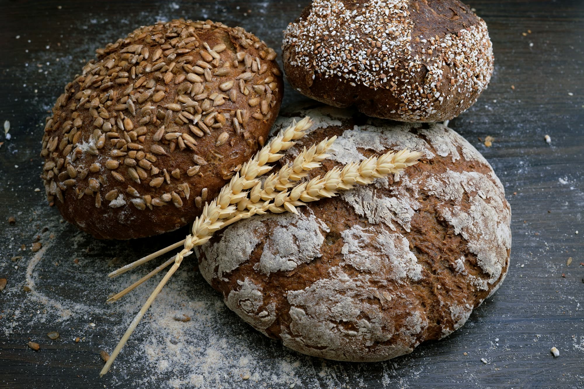 Three dark seeded loaves and ears of wheat on a floured board.