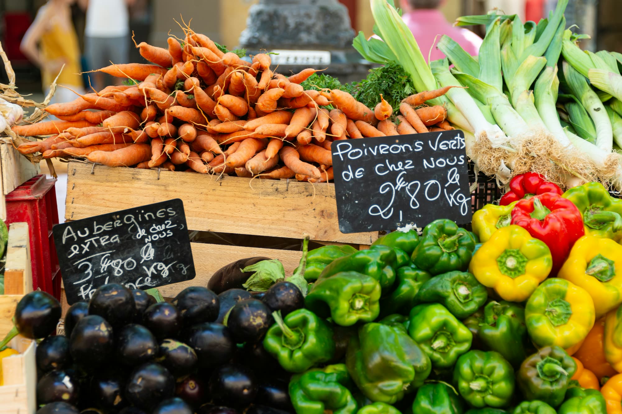 Carrots, aubergines, peppers and leeks in crates on a market stall.